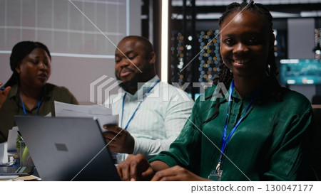 Portrait of smiling black analyst preparing a pitch for important meeting, increasing funds for development after hours. Coworkers team attend a discussion to address goal setting. Camera A. Portrait of smiling black analyst preparing a pitch for important meeting, increasing funds for development after hours. Coworkers team attend a discussion to address goal setting. Camera A. 130047177