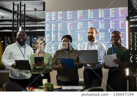 Portrait of multiethnic business team collaborating at night time, assembling in a dark office and working on global company development. Diversity within the advisory board group. Portrait of multiethnic business team collaborating at night time, assembling in a dark office and working on global company development. Diversity within the advisory board group. 130047194