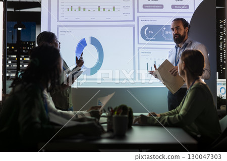 Team of business analysts exchanging project details and forecast data to help achieve business goals, establishing budget and resources allocation. Management team in a night meeting. 130047303