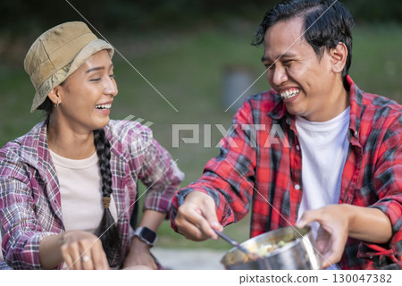 Indonesian southeast asian couple with tongs cooking sliced marinated beef bulgogi on a round grill pan with onions. The scene of the lifestyle of enjoying food in a natural setting Indonesian southeast asian couple with tongs cooking sliced marinated beef bulgogi on a round grill pan with onions. The scene of the lifestyle of enjoying food in a natural setting 130047382