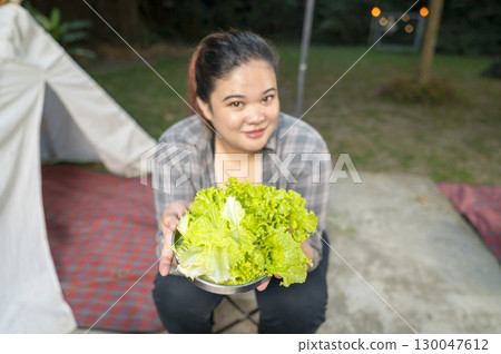 Indonesian southeast asian overweight woman holding a plate of vibrant and fresh green lettuce prepared for a delicious Korean barbecue meal. The scene of lifestyle of enjoying food in natural setting Indonesian southeast asian overweight woman holding a plate of vibrant and fresh green lettuce prepared for a delicious Korean barbecue meal. The scene of lifestyle of enjoying food in natural setting 130047612