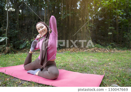 Indonesian southeast asian muslim woman in a sporty outfit practices yoga on a fitness mat in a public park outdoors. Concept of a Healthy active lifestyle 130047669