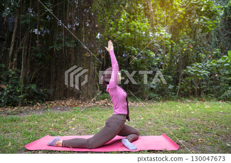 Indonesian southeast asian muslim woman in a sporty outfit practices yoga on a fitness mat in a public park outdoors. Concept of a Healthy active lifestyle 130047673