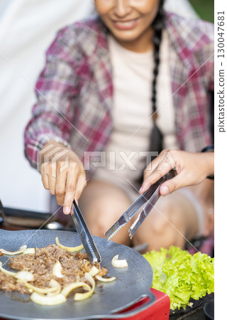 Indonesian southeast asian couple with tongs cooking sliced marinated beef bulgogi on a round grill pan with onions. The scene of the lifestyle of enjoying food in a natural setting Indonesian southeast asian couple with tongs cooking sliced marinated beef bulgogi on a round grill pan with onions. The scene of the lifestyle of enjoying food in a natural setting 130047681