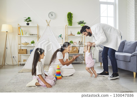 Happy father teaching small toddler girl to walk, playing together in childrens room 130047886