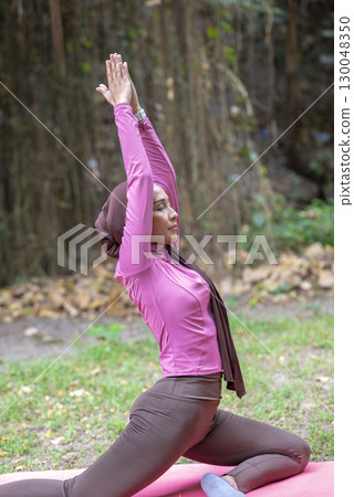 Indonesian southeast asian muslim woman in a sporty outfit practices yoga on a fitness mat in a public park outdoors. Concept of a Healthy active lifestyle 130048350