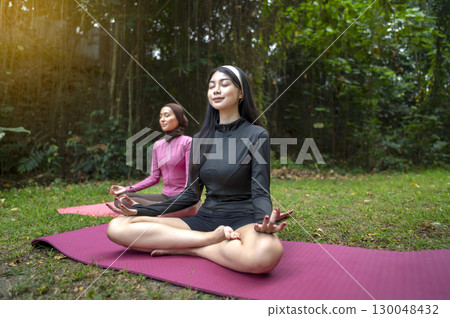 Indonesian southeast asian women in a sporty outfit relaxing and meditating zen-like on a fitness mat in a public park outdoors. Concept of a Healthy active lifestyle 130048432
