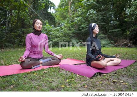 Indonesian southeast asian women in a sporty outfit relaxing and meditating zen-like on a fitness mat in a public park outdoors. Concept of a Healthy active lifestyle 130048434