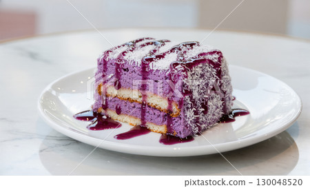 Slice of ube dessert cake with coconut topping and purple syrup on white plate, colorful and sweet Filipino treat 130048520