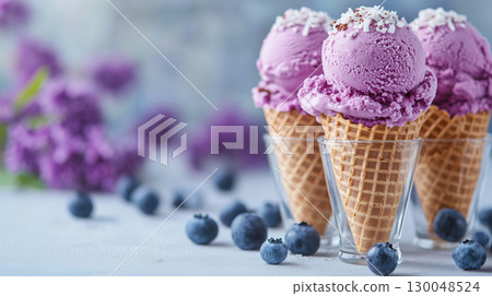 Three cones of blueberry ice cream with shredded coconut topping served in glasses, surrounded by berries and lilac flowers 130048524