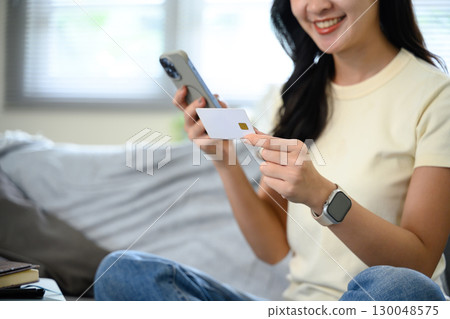 Close up of young woman making mobile payment using debit card and smartphone Close up of young woman making mobile payment using debit card and smartphone 130048575