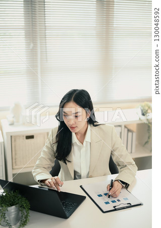 Concentrated female executive checking reports at workplace Concentrated female executive checking reports at workplace 130048592