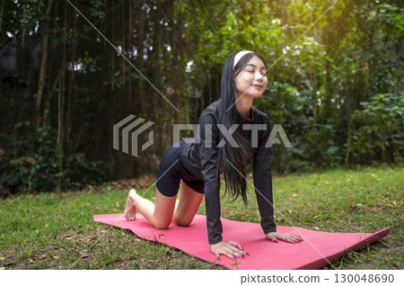 Indonesian southeast asian woman in a sporty outfit practices exercise on a mat in a public park outdoors. Concept of a Healthy active lifestyle Indonesian southeast asian woman in a sporty outfit practices exercise on a mat in a public park outdoors. Concept of a Healthy active lifestyle 130048690