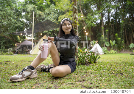 Indonesian southeast asian woman in a sporty outfit holding a drinking bottle after practice running exercise in a public park outdoors. Concept of a Healthy active lifestyle Indonesian southeast asian woman in a sporty outfit holding a drinking bottle after practice running exercise in a public park outdoors. Concept of a Healthy active lifestyle 130048704