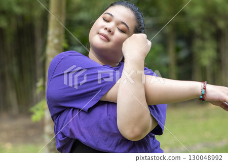 Indonesian southeast asian overweight woman in a sporty outfit practices exercise in a public park outdoors. Concept of a Healthy active lifestyle and body inclusivity 130048992