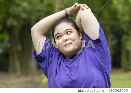 Indonesian southeast asian overweight woman in a sporty outfit practices exercise in a public park outdoors. Concept of a Healthy active lifestyle and body inclusivity 130048993