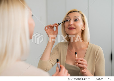 Stylish lady applying volumizing mascara to upper lashes for dramatic look Stylish lady applying volumizing mascara to upper lashes for dramatic look 130049069