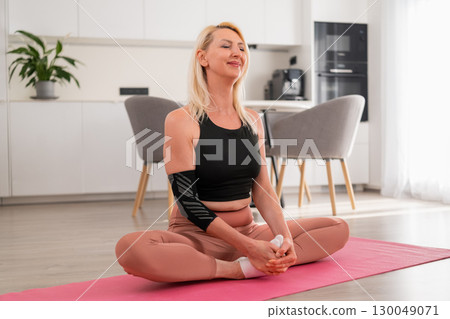 Relaxed blonde woman with close eyes in lotus pose meditating and practicing yoga in contemporary kitchen of modern apartment Relaxed blonde woman with close eyes in lotus pose meditating and practicing yoga in contemporary kitchen of modern apartment 130049071