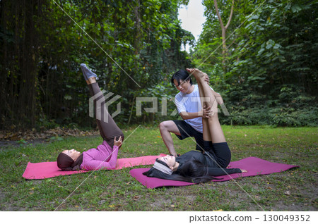 Indonesian southeast asian women in a sporty outfit practice exercise on a mat with a personal trainer man in a public park outdoors. Concept of a Healthy active lifestyle 130049352
