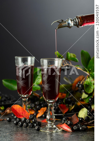 Black chokeberry drink is poured from a bottle into a glass. Black chokeberry drink is poured from a bottle into a glass. 130049597