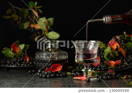 Black chokeberry liquor and fresh berries on a black background. 130049599