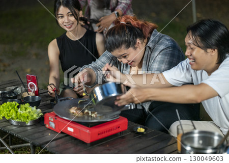Indonesian southeast asian people with tongs cooking sliced marinated beef bulgogi on a round grill pan with onions. The scene of the lifestyle of enjoying food in a natural setting 130049603