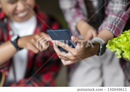 Indonesian southeast asian people enjoying quality time together. Man holds a guitar, and the other women show something on her cellphone. Scene of a lifestyle of enjoying camping in a natural setting Indonesian southeast asian people enjoying quality time together. Man holds a guitar, and the other women show something on her cellphone. Scene of a lifestyle of enjoying camping in a natural setting 130049611
