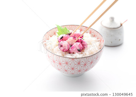 一道日式料理，白飯上鋪著紫蘇、鰹魚和大蒜。餐桌上擺放著醃製的大蒜和紫蘇，色彩繽紛。 130049645