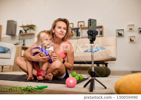 Mother and daughter recording fitness routine together at home for online sharing 130050490