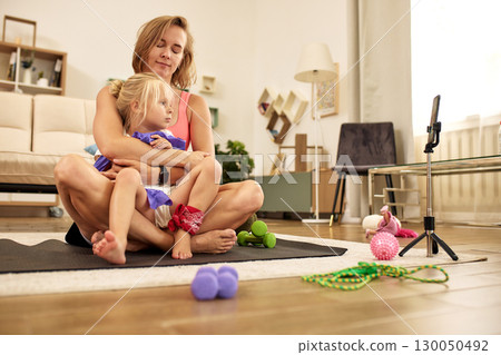 Mother and daughter bonding while exercising in a cozy home setting 130050492