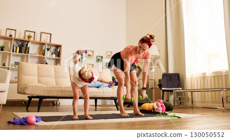 Mother and child exercising with weights together in a cozy living room Mother and child exercising with weights together in a cozy living room 130050552