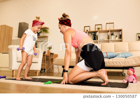 Mother and daughter exercising together on a yoga mat indoors 130050587