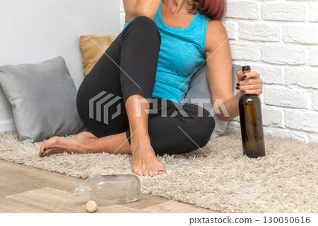Close-up of woman holding bottle of wine sitting on floor at home Close-up of woman holding bottle of wine sitting on floor at home 130050616