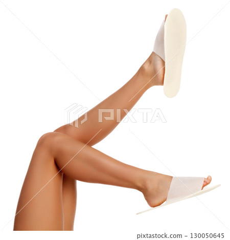 Tanned female legs in white disposable slippers, isolated on white background Tanned female legs in white disposable slippers, isolated on white background 130050645