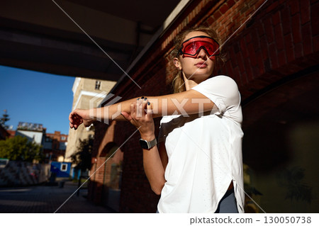 Athletic woman stretching outdoors wearing sporty glasses and smart watch 130050738