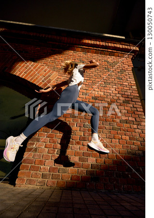 Woman in athletic motion against a brick wall in striking sunlight 130050743