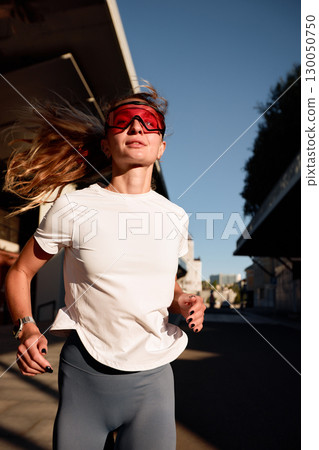 Woman Running Outdoors with Sunglasses under Bright Sunshine 130050750