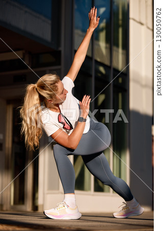 Woman Performing Outdoor Exercise Stretch in Stylish Activewear During Sunset 130050762