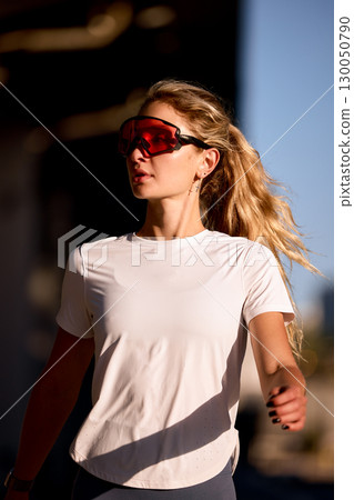 Young woman exercising outdoors wearing sports sunglasses and white activewear shirt 130050790