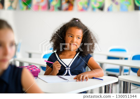 Focused schoolgirl writing notes in classroom. 130051344