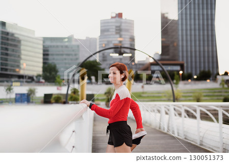 Young woman doing exercise on bridge outdoors in city, stretching. 130051373