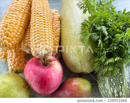 Close-up of fresh vegetables stacked on a table. Corn, zucchini and apples together. A bunch of fresh parsley. 130051988