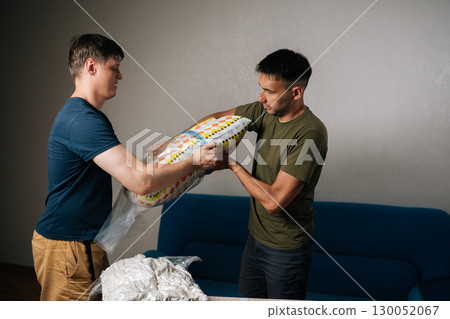 Two movers male using vacuum storage bags to compress bedding and pillows, optimizing space and making moving or storing household items easier. Concept of household chores and housework. 130052067