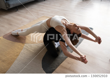 Two women supporting each other in yoga partner pose with balance and mindful stretching indoors. 130052910