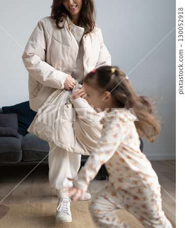 Girl runs across room as mother follows with coat at home 130052918