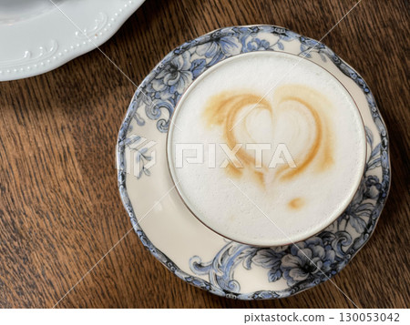 Cappuccino with heart latte art in blue floral cup on wooden table background 130053042