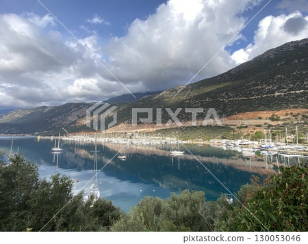 Scenic view of marina with sailboats against mountains and clouds reflecting on water 130053046