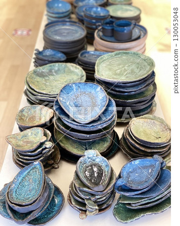 Ceramic tableware with blue green glazed finish stacked on wooden surface 130053048