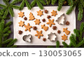 Christmas homemade sweets and decorations. Tradition gingerbreads, cookie cutters, anise stars on baking paper and green spruce frame. 130053065