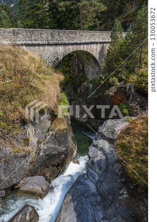 Exploring the serene landscapes of Pyrenees Cauteret with a stone bridge over cascading river at 130053672